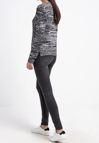 Maglione marled in bianco e nero con scollo rotondo e spacchi laterali. Abbinato a jeans neri slim-fit e sneakers bianche.
