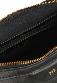 Pochette en cuir noir avec une fermeture éclair dorée et le logo "TED BAKER" embossé sur le côté, dotée d'un intérieur lisse et d'un compartiment zippé.