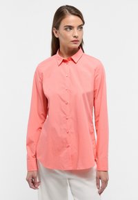 Coral button-up shirt made from lightweight fabric, featuring a pointed collar, long sleeves, and a curved hem. Smooth texture and simple design.