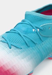 Scarpa da calcio blu chiaro con design a gradiente che passa al rosa. Presenta una tomaia in mesh, lacci piatti e un piccolo logo sul lato.
