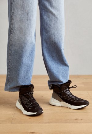 Pantofi scurti negri, căptușiți, cu margine din blană sintetică, superior texturat și talpă din cauciuc alb. Purtați cu blugi lejeri de un albastru deschis.