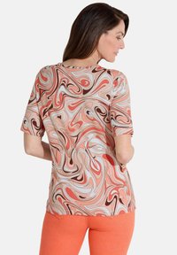 Korte mouwen top in gedraaide oranje, roze en witte patronen, gemaakt van zacht materiaal. Gecombineerd met strakke oranje broek.