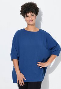 Top blu, oversize, con un tessuto texture, girocollo e maniche corte, abbinato a pantaloni neri. Design semplice e rilassato.