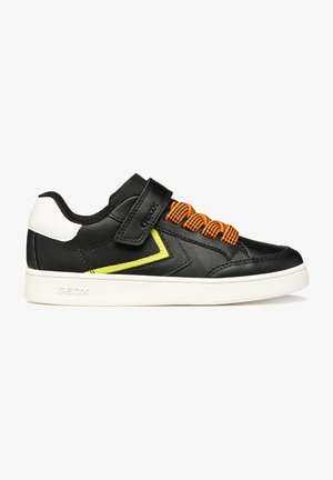 Scarpa da ginnastica nera con suola bianca, lacci arancioni, dettaglio laterale giallo, toppa bianca sul tallone e cinturino in velcro nero sulla parte superiore.