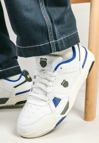 Sneakers bianchi con accenti blu e neri, materiali in pelle e rete, punta traforata e logo sulla linguetta e sul lato.