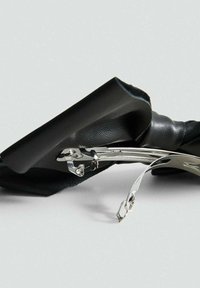 Fermaglio per capelli a fiocco in pelle nera con clasp in metallo argento, aperto, posato su una superficie grigio chiaro.