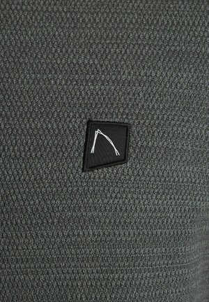 Tessuto a maglia grigio con un motivo testurizzato; presenta un'etichetta in tessuto nera con un design geometrico bianco nell'angolo.