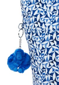 Blå mønstret taske med et geometrisk design i lysere nuancer, med en fuzzy blå gorilla-nøglering hæftet på med en sølvring.