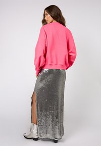 Růžová mikina s volným střihem, doplněná stříbrnou maxi sukní s flitry a rozparkem nad stehnem, a lesklými stříbrnými kotníkovými botami.