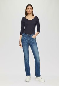 Donker marineblauwe langemouwtop gecombineerd met middelblauwe recht gesneden jeans en witte platform sneakers. Gladde texturen en een getailleerde snit.