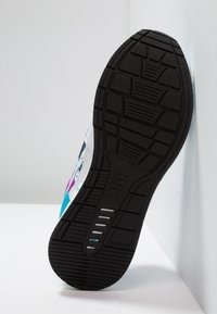 Black rubber sole of a sneaker, textured with grooves and patterns. Upper features white, turquoise, and purple accents.