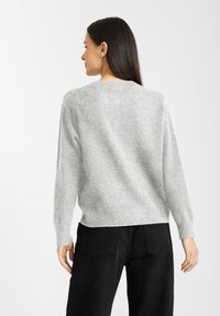 Grijze gebreide trui met een ronde hals en lange mouwen, lichtjes cropped ontwerp, gecombineerd met zwarte broek met hoge taille. Glad textuur.