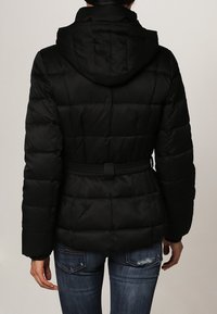 Sort pufferjakke med hætte og bælte i taljen, prydet med et quiltet design og glat, blankt stof. Bagfra ses pæne syninger.