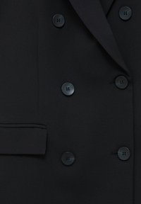 Czarna, dwurzędowa marynarka z sześcioma czarnymi guzikami i kieszenią na klapie po lewej stronie.