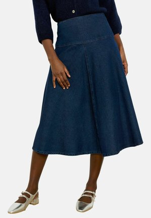 Kobieta ubrana w ciemnoniebieską spódnicę midi z denimu w kształcie litery A z wysokim stanem, w połączeniu z srebrnymi butami Mary Jane i ciemnym swetrem.