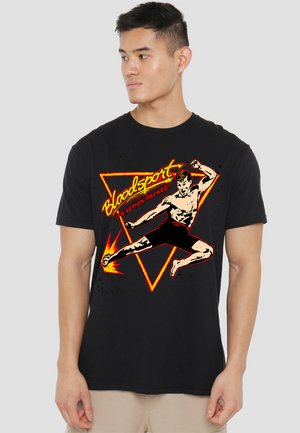 Schwarzes T-Shirt mit einem Grafikmotiv eines männlichen Kämpfers, der mit Flammen tritt, umgeben von einem roten dreieckigen Rahmen und dem Text "Bloodsport" in Gelb.