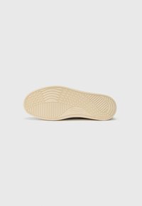Sole de sneaker de un bej deschis, cu un profil ștanțat, caneluri texturate și detalii ridicate, logo în relief și margini netede.
