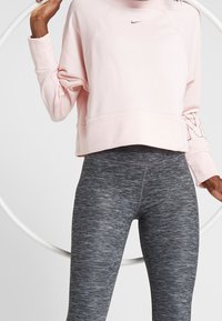 Felpa corta rosa chiaro con un logo discreto, abbinata a leggings a vita alta grigio scuro e texture. Orecchino bianco sullo sfondo.