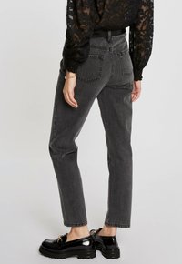 Jeans negros de cintura alta con corte recto, que presentan bolsillos traseros y un acabado texturizado, combinados con mocasines negros brillantes.