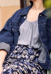 Denimjakke med sølvknapper, grå bluse med plissering og blomstertryk-skirt i navy, lyseblå og beige toner.