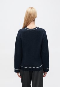 Pull bleu marine avec une finition texturée, doté d'un col rond et de surpiqûres blanches en accent le long de l'encolure et de l'ourlet.