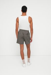 Pantaloni corti neri con un motivo circolare bianco, vita elasticizzata, tasca posteriore, indossati con una canotta bianca e abbinati a sneakers bianche e calze chiare.