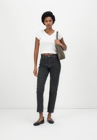 White cropped V-neck top, high-waisted black jeans, and black flats. Holding a dark green handbag. Smooth textures, simple design.