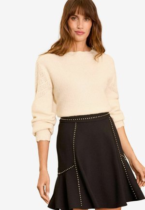 Cream, ribbed knit sweater with a round neck and patterned sleeves paired with a black skirt featuring studded accents and a flared hem.