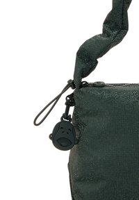Donkergroene pouch tas met een gestructureerd, gaasachtig patroon, voorzien van een rits en een ronde ritsenhanger in de vorm van een aap.