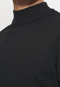 Mustapaita, jossa on ribattua korkeaa kaulaa. Valmistettu neulotusta kankaasta, joka näyttää sileältä ja istuvalta. Ei näkyviä kuvioita tai metalliosia.