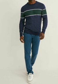 Mörkblå stickad tröja med gröna och vita horisontella ränder, i kombination med tealfärgade byxor och vita sneakers. En enkel, avslappnad outfit.