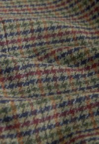 Tkanina wełniana w wzór houndstooth w zielonych, czarnych i czerwonych odcieniach, z teksturowaną powierzchnią i miękkimi włóknami.