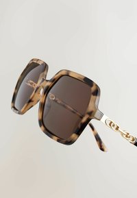 Ochelari de soare hexagonali cu lentile întunecate, în nuanță de scoică țestoasă, decorați cu detalii din lanț auriu pe brațe și finisaj lucios.