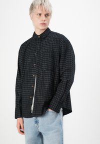 Chemise à carreaux noirs avec col, dotée d'une poche poitrine et de manches longues, assortie à un jean en denim bleu clair.