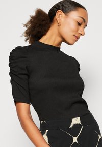 Black pullover top with short, puffed sleeves and a textured fabric. Features a high neck and fitted silhouette.