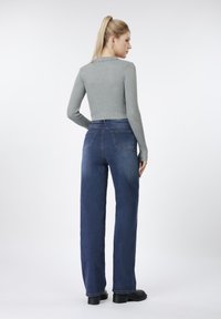 Γκρι μακρυμάνικη μπλούζα με ραβδώσεις, συνδυασμένη με σκούρα μπλε τζιν παντελόνι φαρδύ στο κάτω μέρος, με κλασικό σχέδιο πέντε τσεπών και κλείσιμο με φερμουάρ.