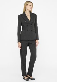 Completo grigio scuro a righe finemente dettagliato con giacca doppiopetto, revers a punta e pantaloni abbinati. Presenta bottoni neri e una silhouette elegante.