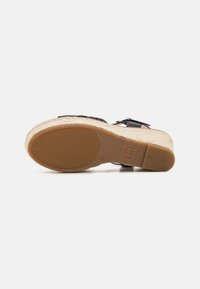 Sandal de esparto negro con parte superior trenzada, suela envuelta en yute, suela de goma y hebilla ajustable. Presenta una plantilla texturizada.