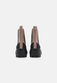 Mustat ja vaaleanbeiget nilkkurit, joissa on teksturoituja paneeleja, paksut pohjat ja vetonauhat takana helppoa pukemista varten. Sileä synteettinen materiaali.