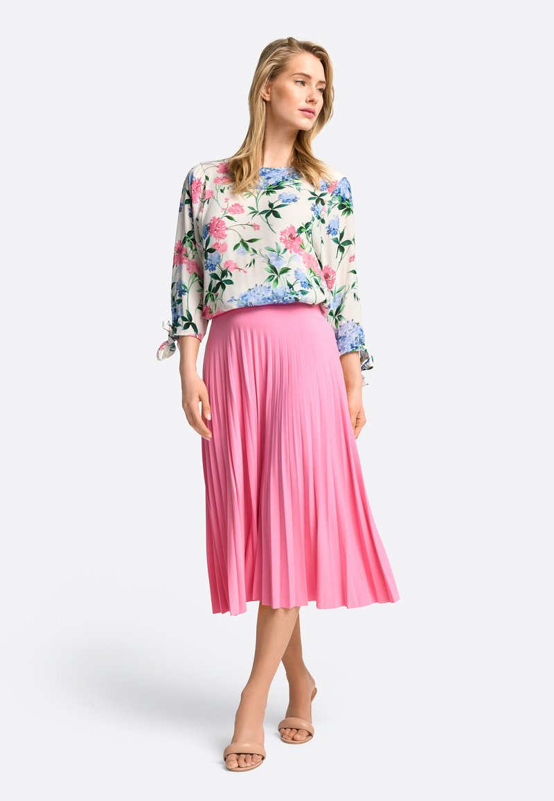 Blumenbluse mit rosa Plisseerock. Die Bluse hat blaue und rosa Blumen auf einem weißen Stoff. Der Rock ist lang und fließend; glatte Textur.