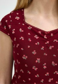 Bordeaux topp med korte ærmer, der har et blomstermønster af små lyserøde roser og grønne blade, accentueret med en blondekant ved udskæringen.