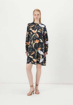 Abito nero con stampa floreale colorata, maniche lunghe e vestibilità rilassata. Indossato con sandali con tacco beige. Texture morbida, design casual.