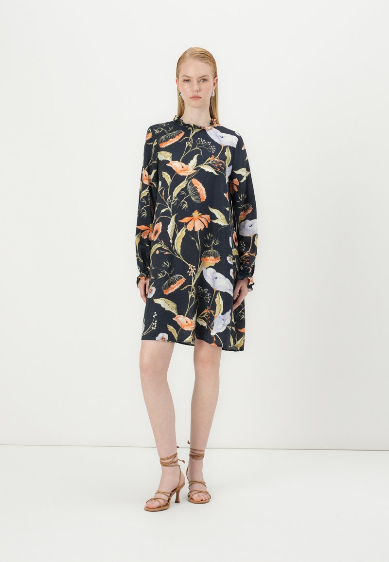 Vestido preto com padrão floral colorido, mangas compridas e corte descontraído. Usado com sandálias de salto bege. Textura suave, design casual.