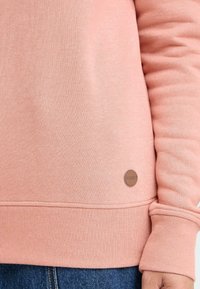 Felpa color pesco realizzata in morbido cotone misto. Presenta polsini e orlo a coste, con una piccola etichetta logo marrone sul lato sinistro in basso.