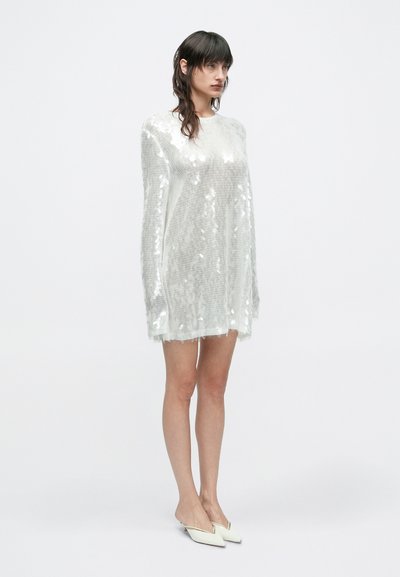 Διάφανο, φαρδύ φόρεμα καλυμμένο με ασημένιες πα�γιέτες, με στρογγυλή λαιμόκοψη και ξεφτισμένο τελείωμα, συνδυασμένο με λευκά μυτερά φλατ παπούτσια.