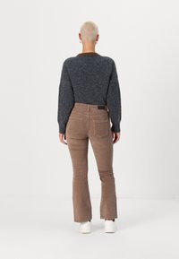 Grå tröja med brunt krage, kombinerad med ljusbruna kordbyxor med utsvängda ben. Vita sneakers fulländar outfiten. Bakifrån.