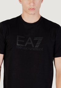 T-shirt nera a maniche corte con logo EA7 Emporio Armani in rilievo ricamato in nero abbinato. Realizzata in tessuto morbido con una vestibilità classica.