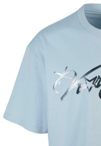 Heleline sinine puuvillane T-särk, millel on lühikesed varrukad, ümmargune kaelus ja metallist hall graafiline disain koos tekstiga ning tähe aktsentidega.