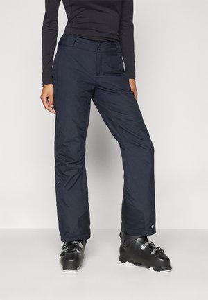 Navy ski pants made of waterproof material, featuring a straight fit, two side pockets, and reinforced lower panels. Paired with black ski boots.