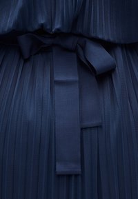 Πλισέ ύφασμα σε ναυτικό μπλε με μια φαρδιά υφασμάτινη κορδέλα δεμένη σε χαλαρό φιόγκο στο κέντρο.